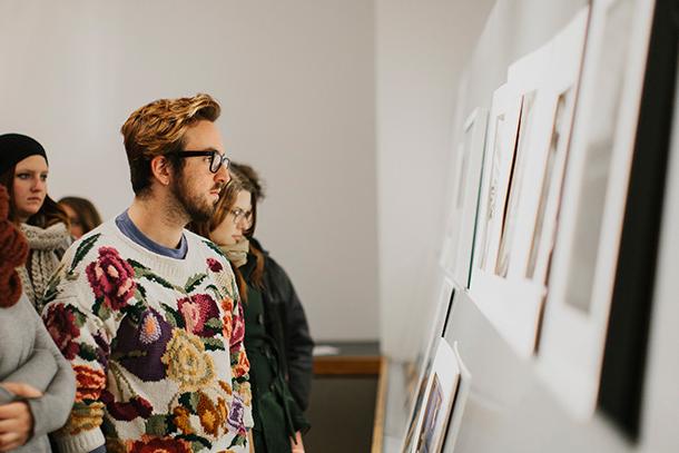 student with glasses and floral sweater examining artwork mounted to wall