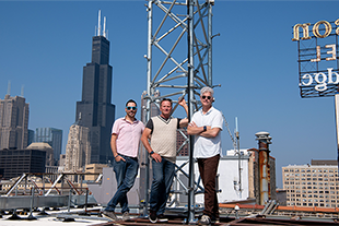 三个人站在屋顶上，身后有一座塔
